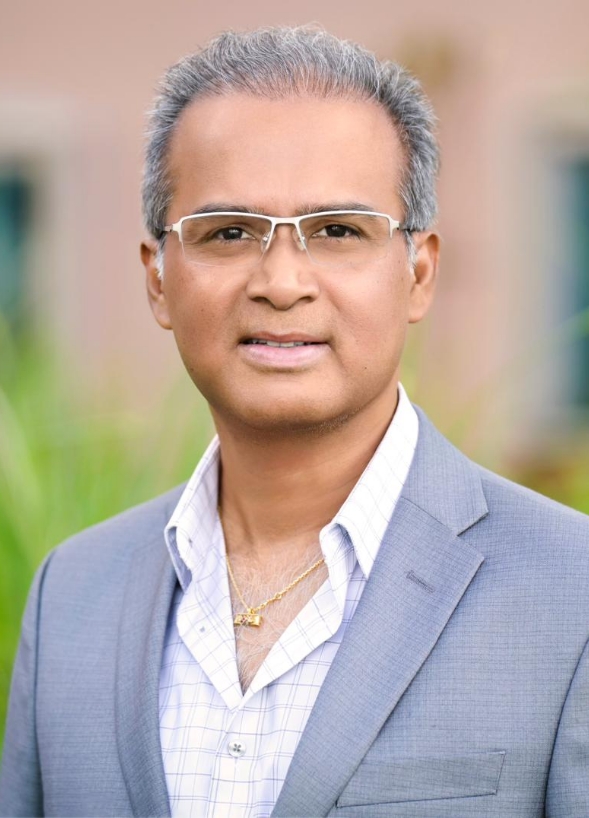 Professional portrait of a middle aged man in a light gray suit and white shirt wearing glasses outdoors